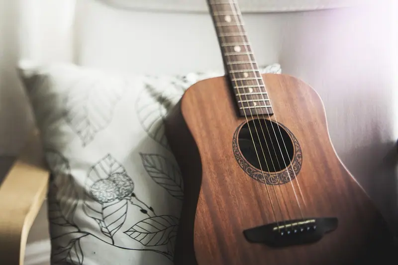 Violão encostado numa almofada, perto de uma janela com luz do dia