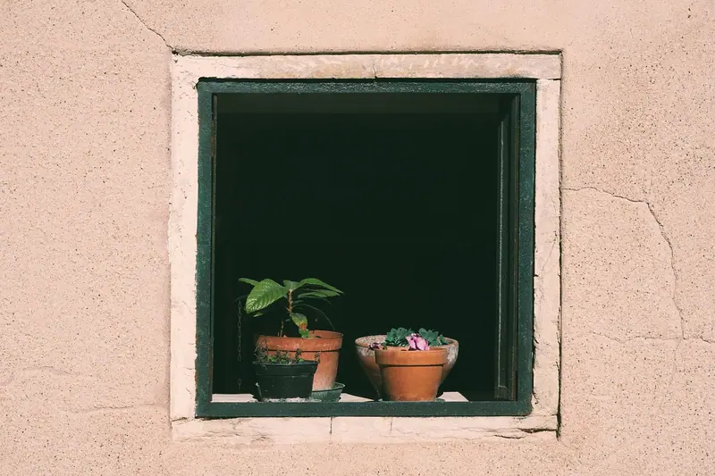 Janela recuada numa parede grossa rosada, com vasos de plantas apoiados no peitoril