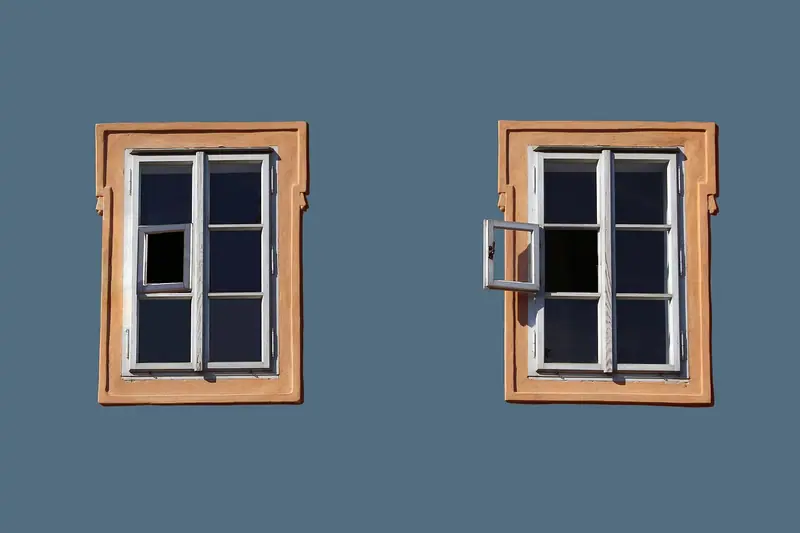 Duas janelas com moldura de madeira numa parede azul, uma fechada e outra com uma folha aberta