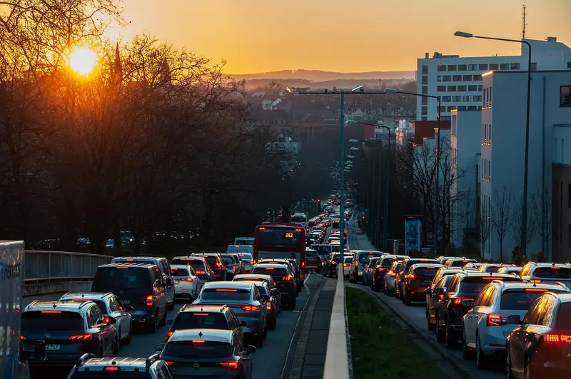 Avenida congestionada ao pôr do sol, com filas de carros nos dois sentidos e prédios ao lado