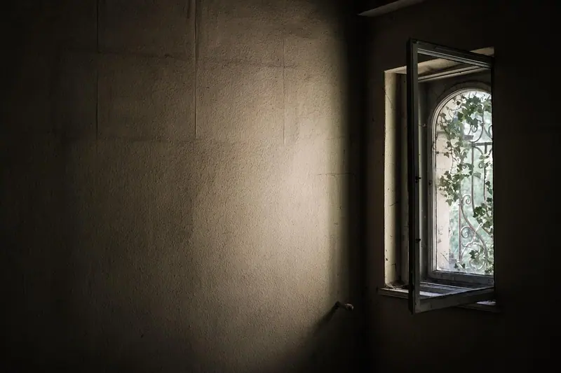 Quarto escuro com uma janela de abrir entreaberta deixando entrar a luz do dia
