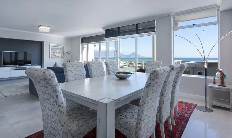 Sala de jantar de apartamento com janelões fechados e vista para o mar e os morros