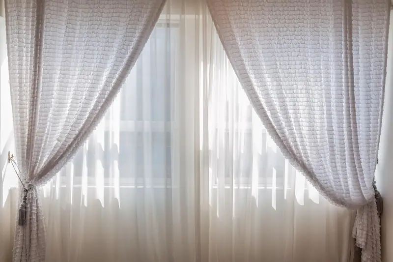 Janela com cortina branca de renda presa nas laterais, deixando entrar a luz do dia