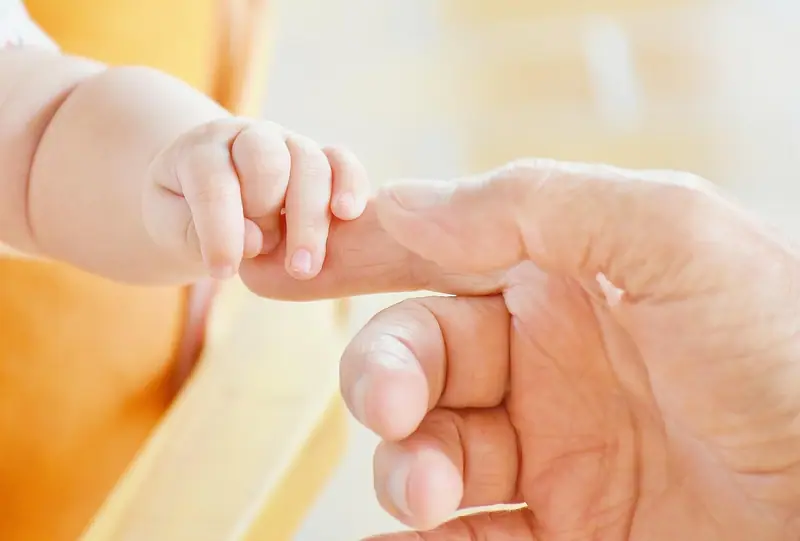 Mão pequena de bebê segurando o dedo de um adulto, em luz suave