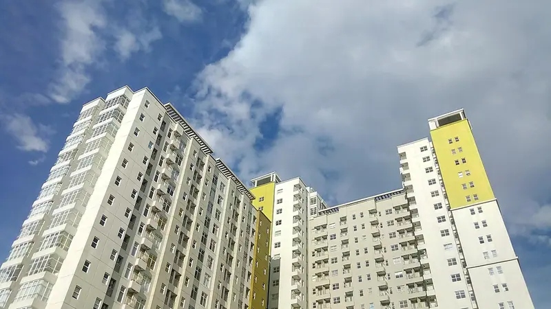 Dois prédios residenciais altos, com fileiras de janelas iguais, vistos de baixo num dia de nuvens