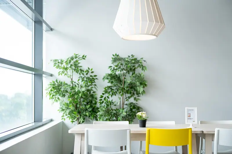 Sala clara com mesa branca, cadeira amarela, plantas e uma janela ampla na lateral