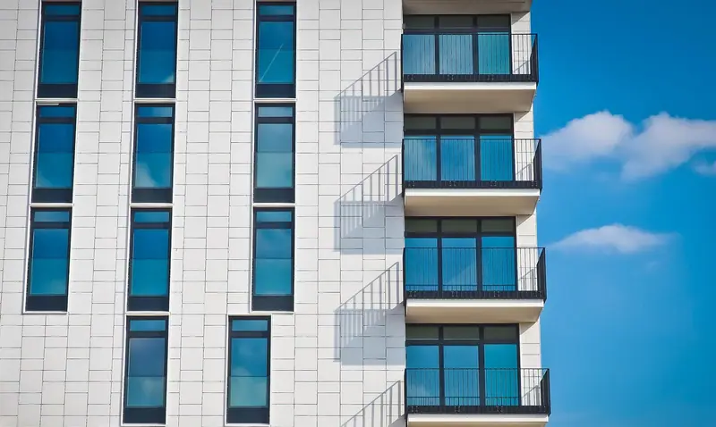 Fachada de prédio residencial branco com varandas e janelas de vidro sob céu azul