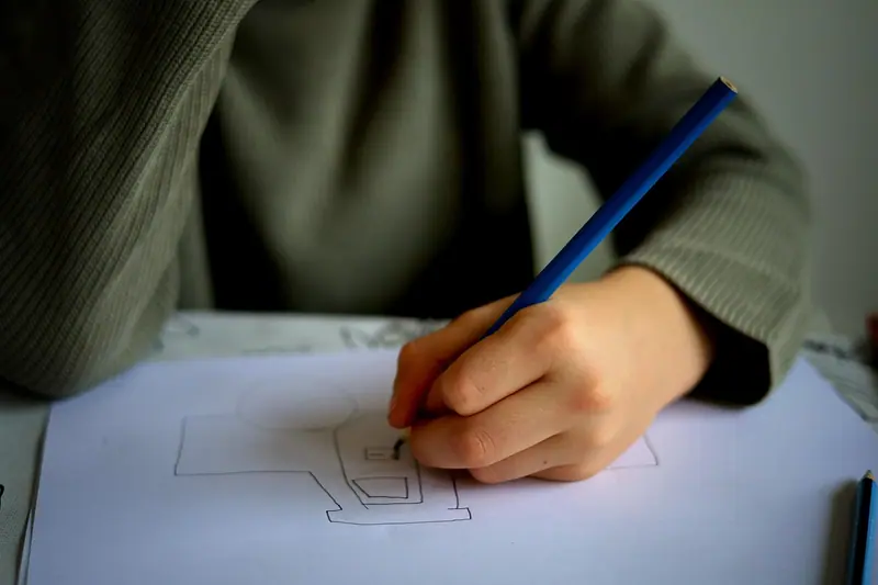 Mão desenhando com lápis azul o esboço de uma planta numa folha branca sobre a mesa