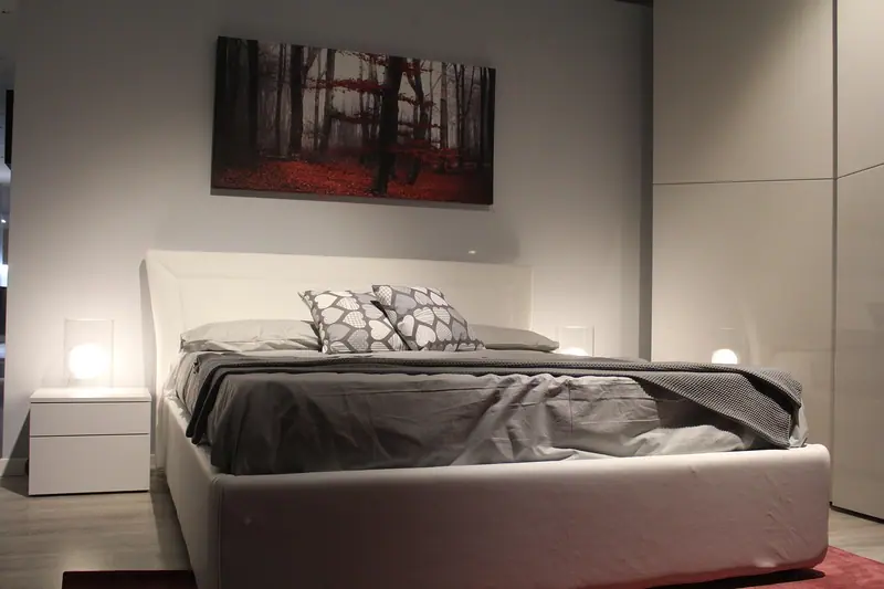 Quarto com cama de casal, abajures acesos e guarda-roupa branco ocupando a parede lateral