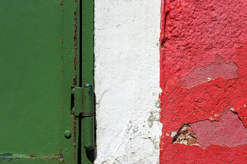 Dobradiça de uma porta de metal verde, junto a uma parede pintada de branco e vermelho