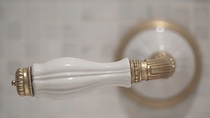 Maçaneta de porcelana branca com acabamento dourado, vista de perto diante de uma porta clara
