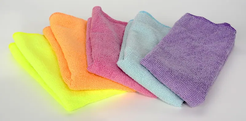 Panos de microfibra dobrados em amarelo, laranja, rosa, azul e lilás sobre fundo claro