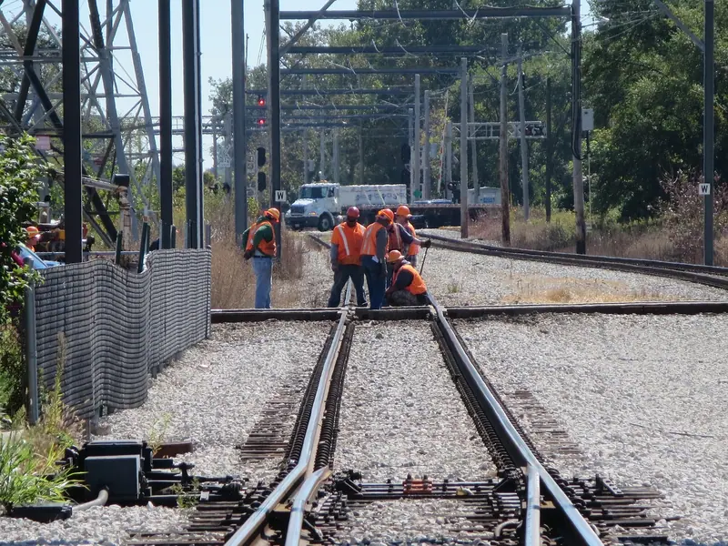 Trabalhadores de colete laranja reunidos sobre um aparelho de mudança de via, onde os trilhos se dividem