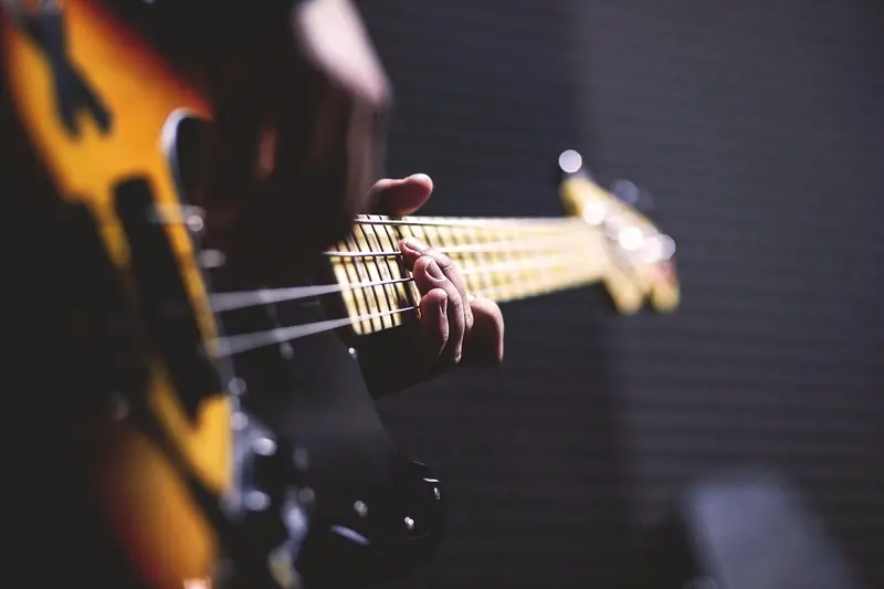 Mãos tocando um contrabaixo diante de uma parede revestida de espuma escura