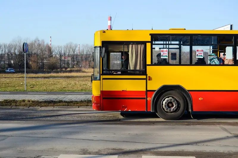 Ônibus urbano amarelo e vermelho passando por uma rua, visto de lado