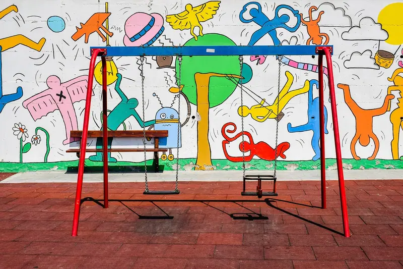 Pátio vazio com um balanço vermelho na frente de um muro pintado com desenhos coloridos