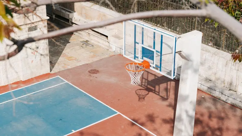 Quadra de basquete vazia vista do alto, com piso azul e vermelho e a tabela ao lado