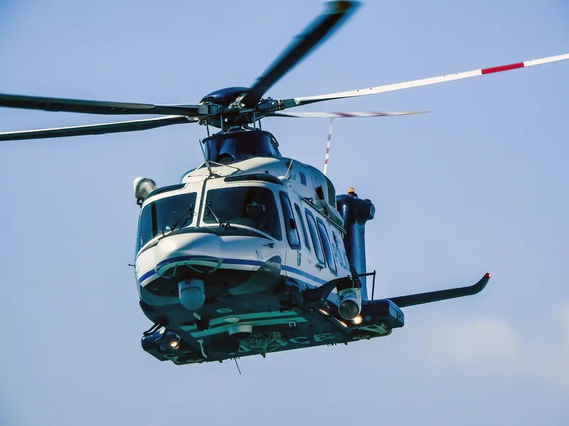 Helicóptero branco em voo, visto de frente, com as pás do rotor girando