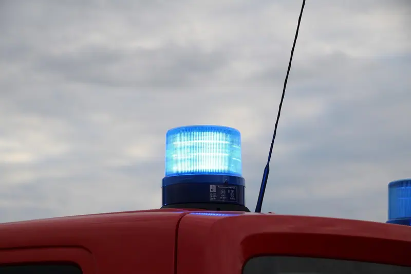 Luz giratória azul acesa no teto de um veículo de emergência vermelho, contra o céu nublado