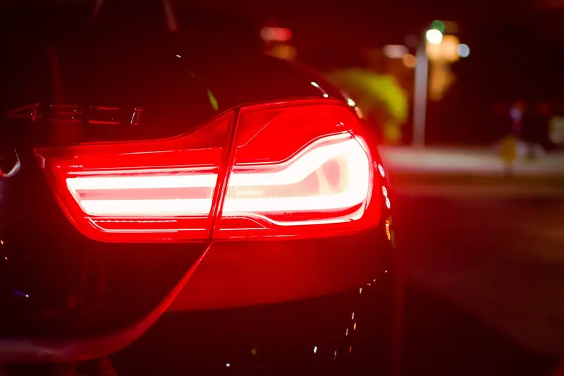 Lanterna traseira de um carro acesa em vermelho, vista de perto numa rua à noite