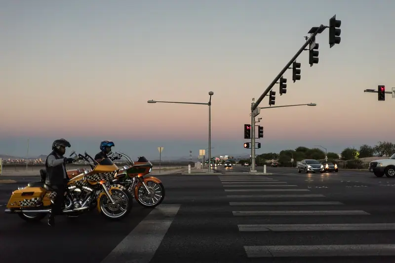 Duas motos paradas na faixa diante de um semáforo, ao entardecer, com os pilotos de capacete