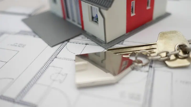 Maquete de casa branca e vermelha com um molho de chaves sobre a planta baixa de um imóvel