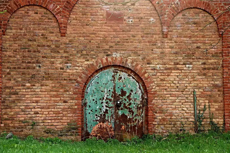 Muro alto de tijolos aparentes com um portão de metal em arco, fechado