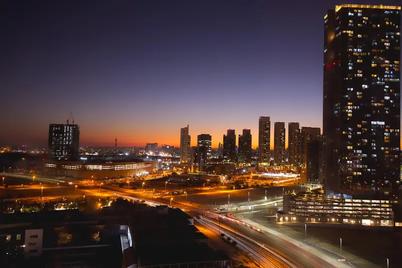 Cidade ao anoitecer, com prédios altos e avenidas iluminadas pelo trânsito