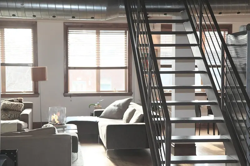 Sala com sofás claros ao lado de uma escada de metal que leva ao andar de cima