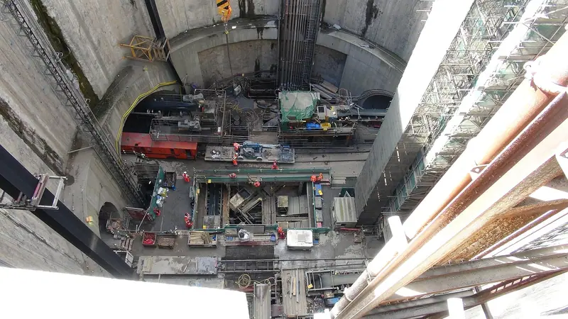 Vista de cima de um poço de obra subterrânea, com estruturas metálicas e equipamentos no fundo
