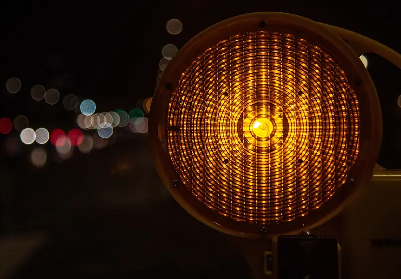 Sinalizador amarelo de obra aceso à noite, com luzes da rua desfocadas ao fundo