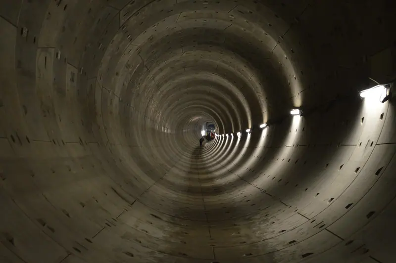 Túnel circular revestido de anéis de concreto, iluminado por lâmpadas nas paredes