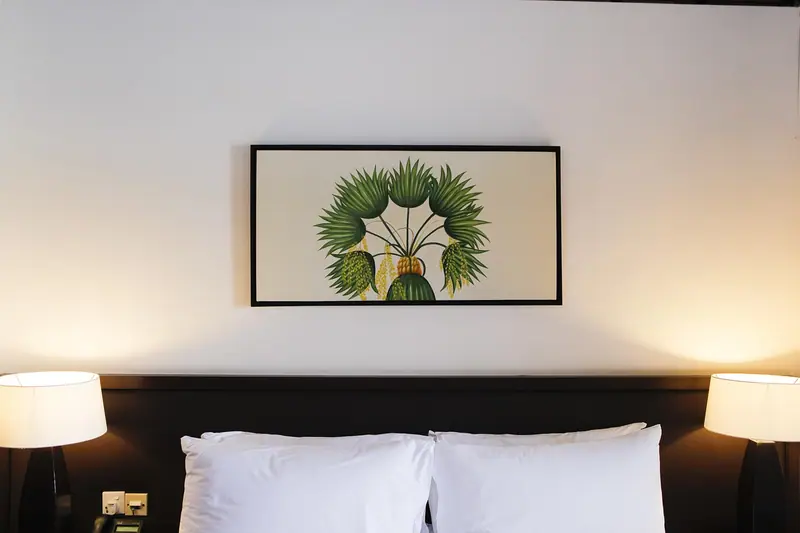Cama com travesseiros brancos e cabeceira escura encostada numa parede com um quadro