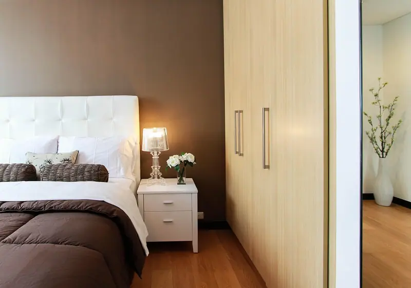 Quarto com cama de casal ao lado de um guarda-roupa de madeira que ocupa a parede
