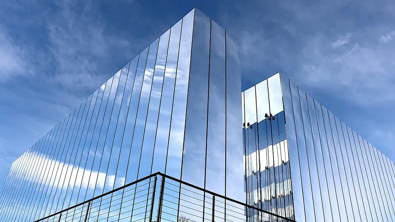 Prédio com fachada de vidros espelhados refletindo o céu azul e as nuvens
