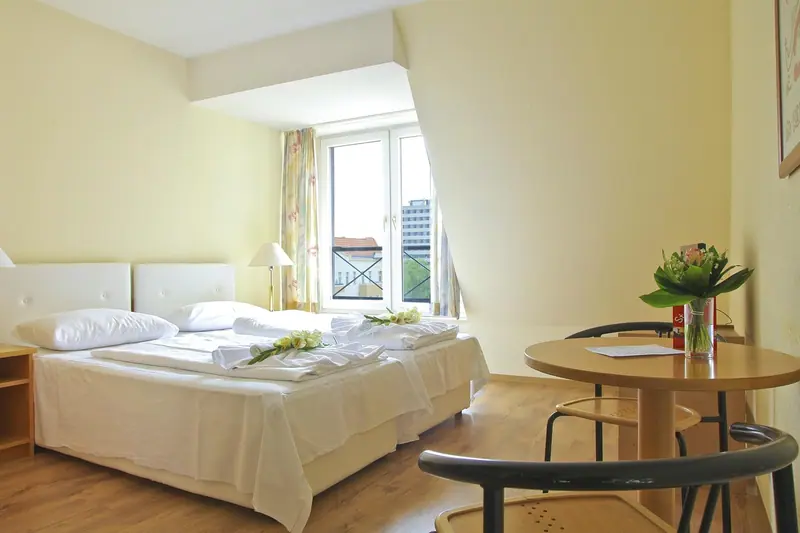 Quarto claro com duas camas, mesa redonda e porta de vidro para a varanda