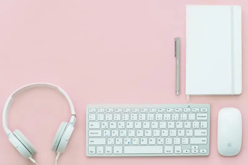 Fones de ouvido brancos ao lado de um teclado, um mouse e um caderno