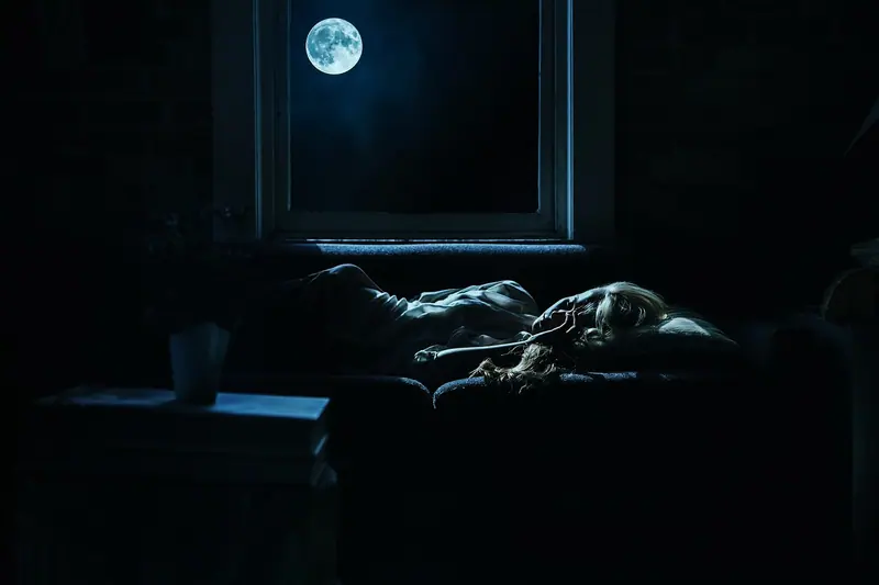 Pessoa deitada num sofá em um cômodo escuro, iluminada só pela luz da lua que entra pela janela