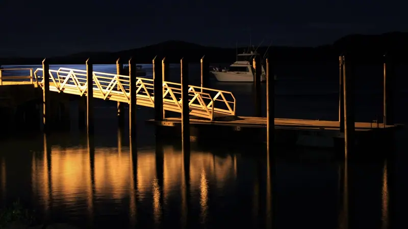Píer iluminado sobre um lago escuro à noite, com as luzes refletidas na água parada