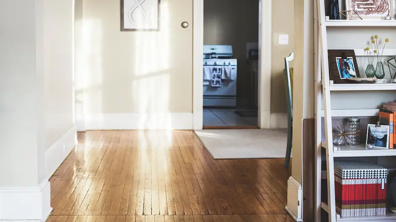 Corredor de apartamento com piso de madeira, paredes claras e uma porta aberta ao fundo