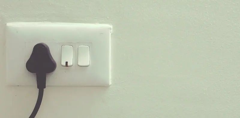 Tomada com um plugue conectado e interruptor duplo numa parede clara