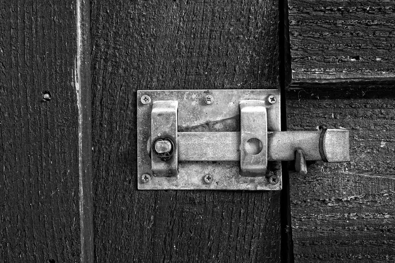 Ferrolho de metal prateado fechado numa porta de madeira pintada de preto