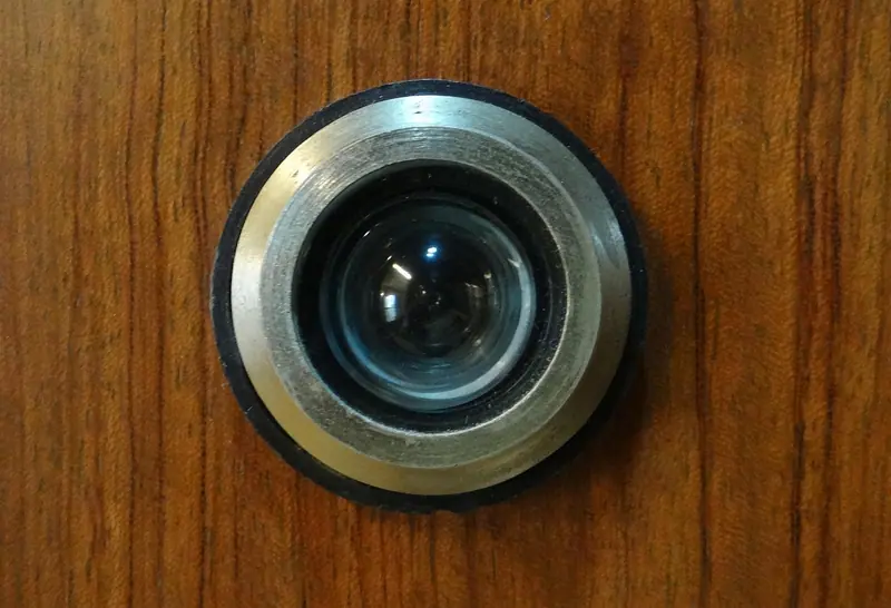 Olho mágico de metal prateado numa porta de madeira, visto de perto