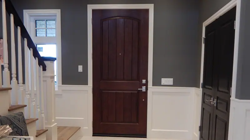 Porta de madeira escura num hall de entrada claro, ao lado de uma escada com corrimão branco