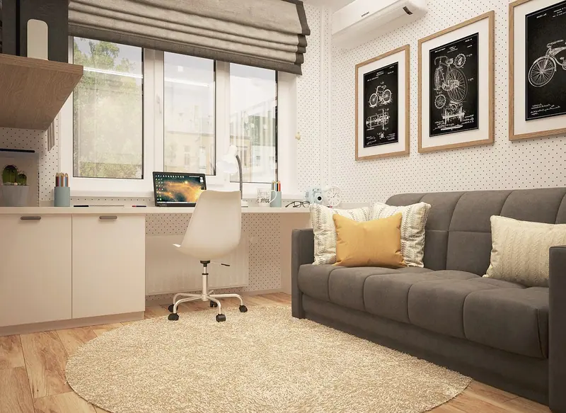 Cômodo de home office com mesa e cadeira junto à janela, sofá cinza e quadros na parede