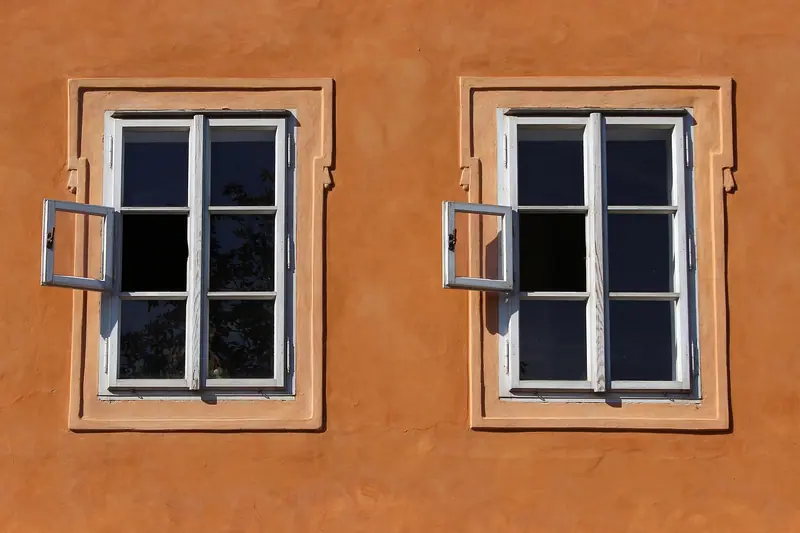 Duas janelas de madeira branca abertas numa fachada pintada de laranja