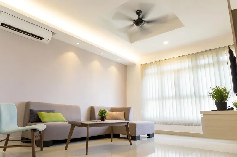Sala clara com ar-condicionado na parede, ventilador de teto, sofá e cortinas na janela