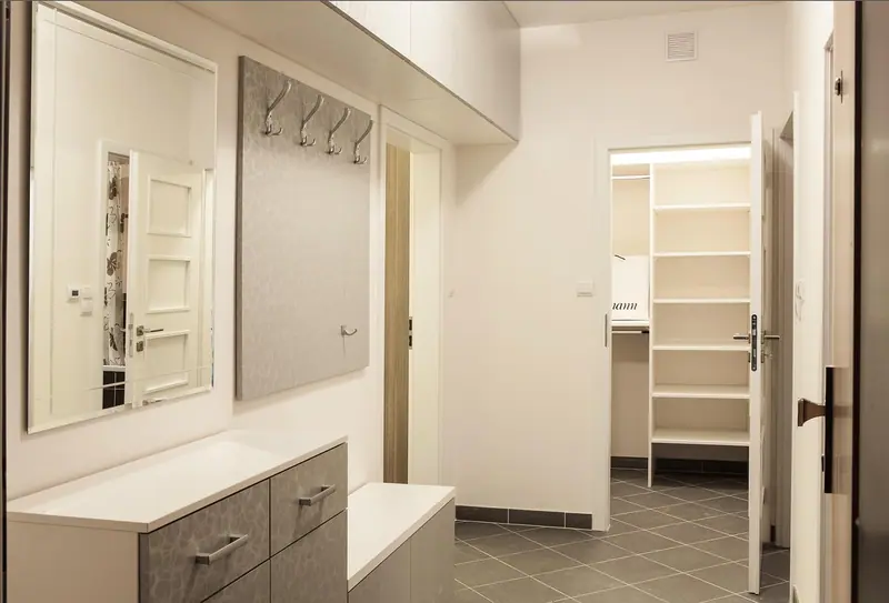 Hall de entrada de um apartamento com portas brancas, armário e piso cinza