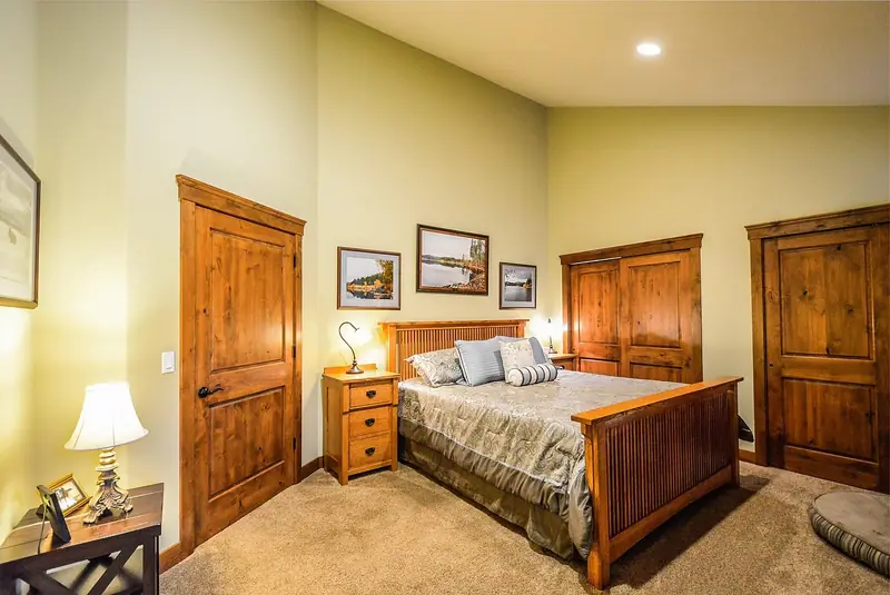 Quarto com cama de madeira, abajures nas mesas de cabeceira e duas portas de madeira fechadas