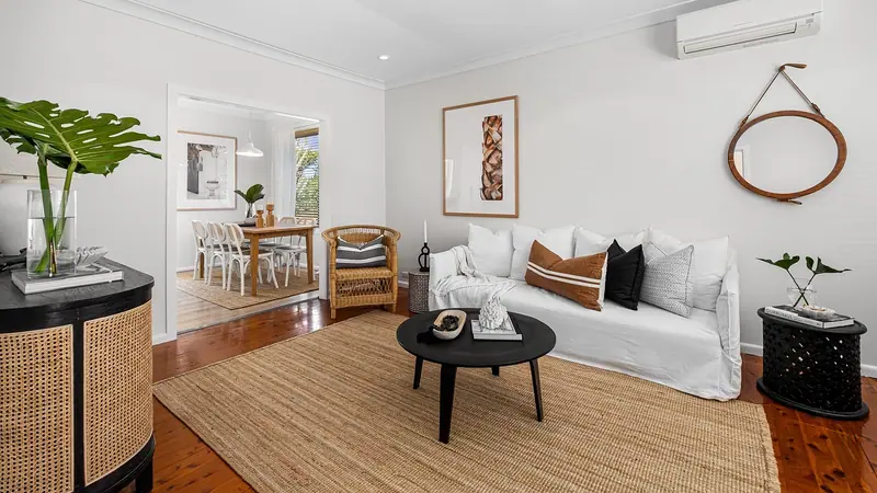 Sala clara com sofá branco, tapete de fibra e ar-condicionado no alto da parede, com passagem para a sala de jantar